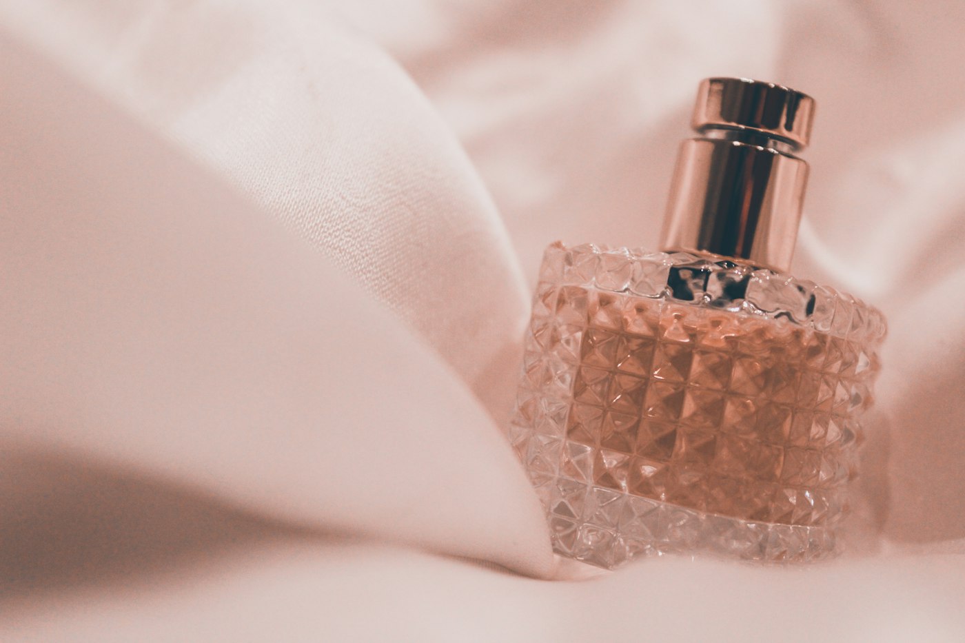 Faceted glass perfume bottle on blush silk