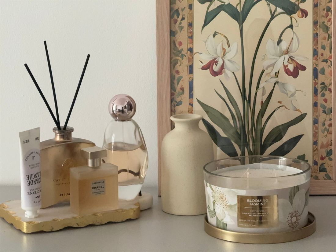 Perfume bottles, a reed diffuser and a jasmine candle in front of an orchid print